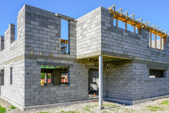Construction d'une maison individuelle en cours, murs en blocs de béton cellulaire gris, structure à deux niveaux avec ouvertures pour portes et fenêtres