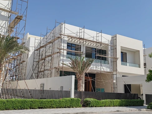 Chantier de rénovation extérieure d'une maison individuelle à deux étages avec échafaudage métallique rouge installé sur la façade
